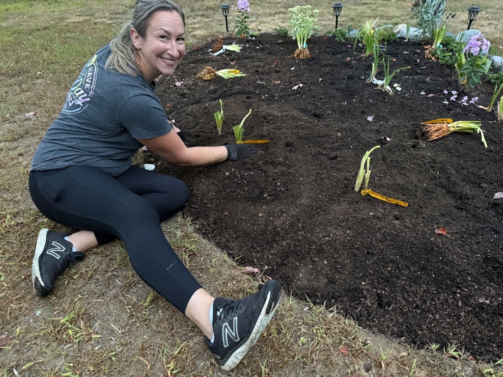 Woman smiling while planting daylilies in a fresh garden bed at night