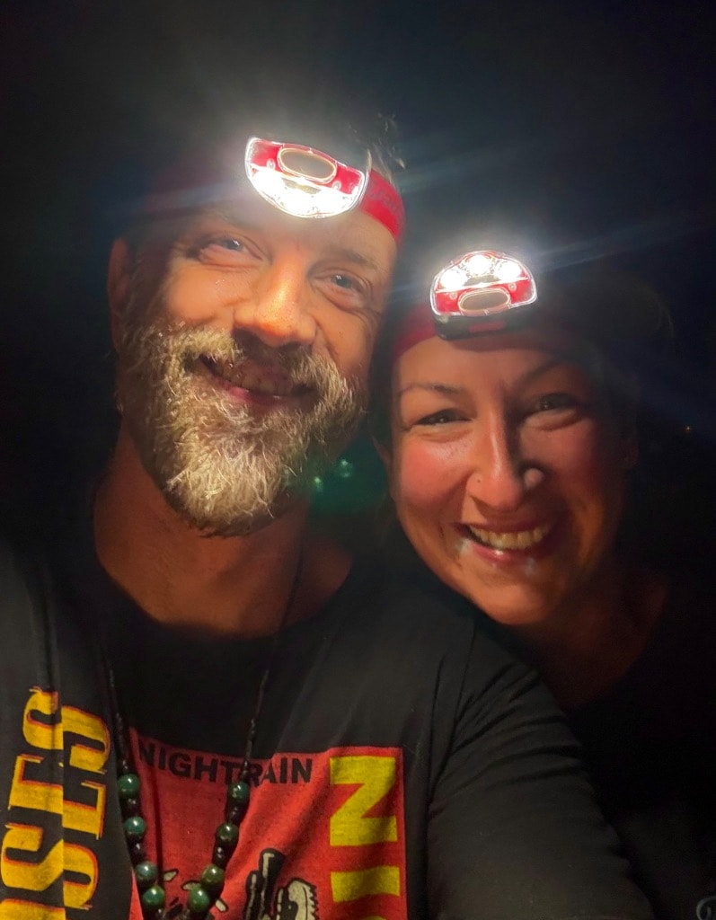 Two people wearing red headlamps smiling at night after planting daylilies until midnight